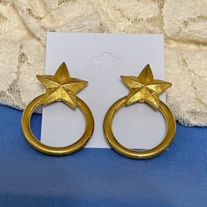 May include: A pair of gold-toned earrings featuring a star-shaped charm on a circular hoop.