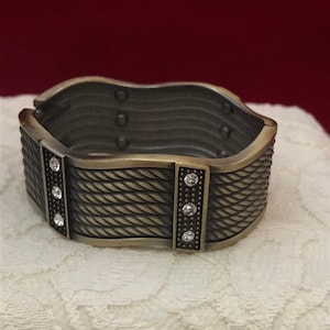 May include: A silver-toned bangle bracelet with a rope-like design and clear crystal accents.