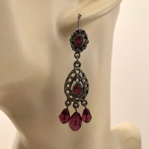 Può includere: Orecchini pendenti in argento con un design a forma di lacrima e tre cristalli viola pendenti.