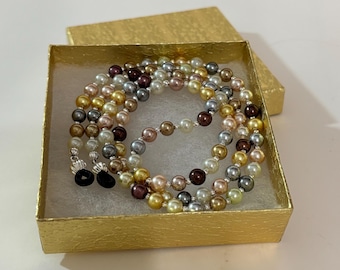 May include: A multi-coloured pearl eyeglass chain with black silicone ends in a gold gift box. The chain is made of small, round pearls in shades of gold, brown, grey, and white.