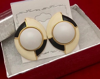 May include: A pair of white and black geometric clip-on earrings with gold accents. The earrings have a white center with a black and white geometric design around it.
