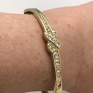 May include: A gold bangle bracelet with a knot design and clear rhinestones.