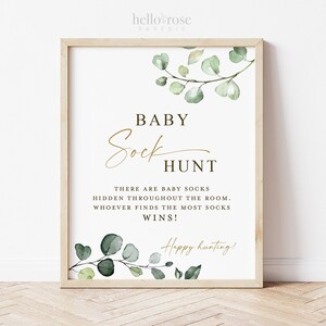 May include: A printable sign with a green eucalyptus leaf design and the text "BABY Sock HUNT" in gold lettering. The sign reads "There are baby socks hidden throughout the room. Whoever finds the most socks wins! Happy hunting!"