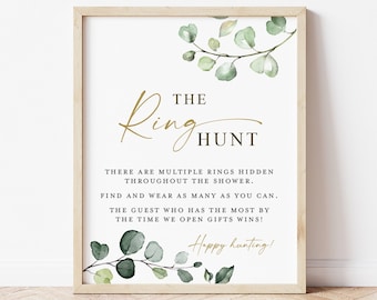 May include: A framed sign with the text "The Ring Hunt" in gold script, with instructions for a game. The sign is decorated with watercolor eucalyptus leaves and branches. The sign is on a white background.