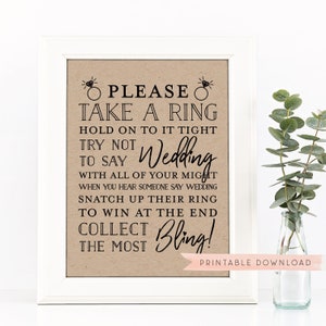 Può includere: Un cartello stampabile con sfondo marrone e testo nero che dice "PLEASE TAKE A RING HOLD ON TO IT TIGHT TRY NOT TO SAY Wedding WITH ALL OF YOUR MIGHT WHEN YOU HEAR SOMEONE SAY WEDDING SNATCH UP THEIR RING TO WIN AT THE END COLLECT Bling! THE MOST" e "PRINTABLE DOWNLOAD" in basso.