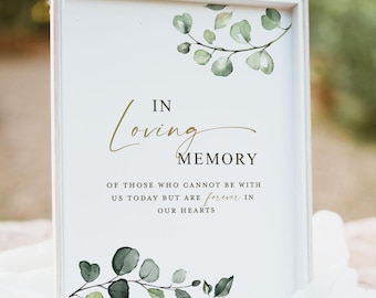 Op de afbeelding: Een wit ingelijst bord met aquarel eucalyptusbladeren aan de boven- en onderkant. De tekst luidt: IN Loving MEMORY OF THOSE WHO CANNOT BE WITH US TODAY BUT ARE forever IN OUR HEARTS. De lijst is gemaakt van lichtgekleurd hout.