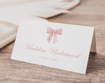May include: White place card with a pink watercolor bow and the text "Madeline Underwood" and "Table One".