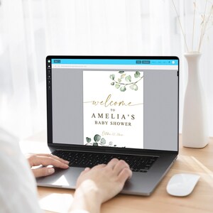 Puede incluir: Un dise&ntilde;o digital para un cartel de bienvenida de baby shower con un dise&ntilde;o de rama de eucalipto en acuarela y texto dorado que dice "Bienvenido al baby shower de Amelia, 22 de octubre de 2023".