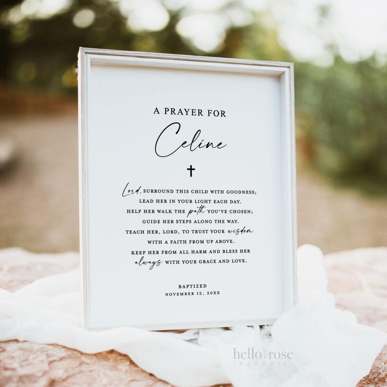 May include: A white framed print with a black cross and the text "A Prayer for Celine" and a prayer for the child. The text reads "Lord, surround this child with goodness; lead her in your light each day. Help her walk the path you've chosen; guide her steps along the way. Teach her, Lord, to trust your wisdom. With a faith from up above. Keep her from all harm and bless her always with your grace and love." The print also includes the text "Baptized November 12, 20XX".