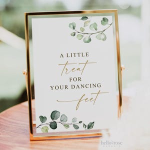 May include: A white sign with gold lettering and a green watercolor floral design. The sign reads "A little treat for your dancing feet".
