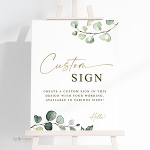 May include: A white sign with a gold script font that says "Custom Sign". The sign also includes the text "Create a custom sign in this design with your wording. Available in various sizes!" and a small green eucalyptus branch with the word "Hello!" in gold script font.
