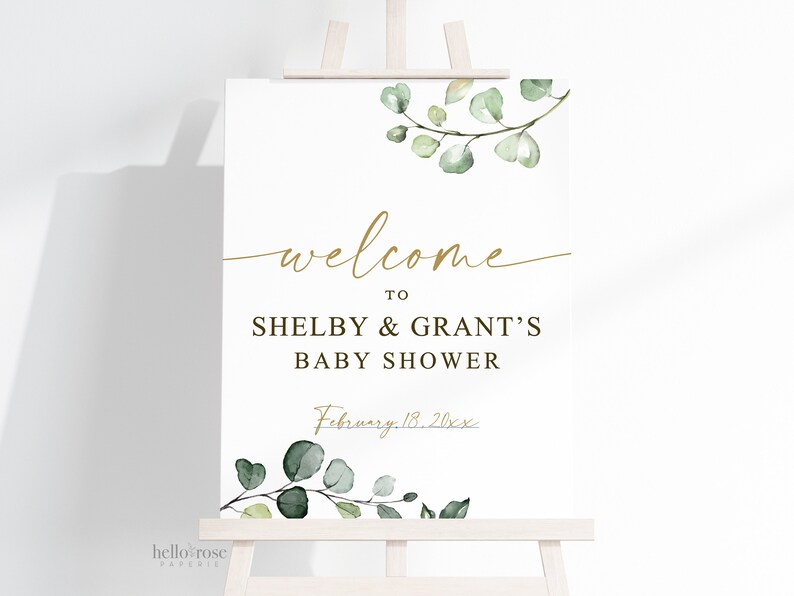 Puede incluir: Un cartel de bienvenida blanco con letras doradas y hojas verdes de acuarela. El cartel dice "Bienvenido a Shelby & Grant's Baby Shower, 18 de febrero de 20xx".