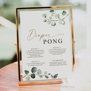 May include: A white sign with green foliage illustrations and gold text. The sign has instructions for a game called "Diaper Pong" with three rounds and a tiebreaker.