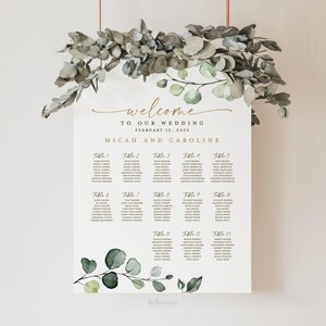 May include: A wedding seating chart with a eucalyptus and greenery design. The chart is printed on white cardstock and features the text "Welcome to our wedding, February 12, 2023, Micah and Caroline".