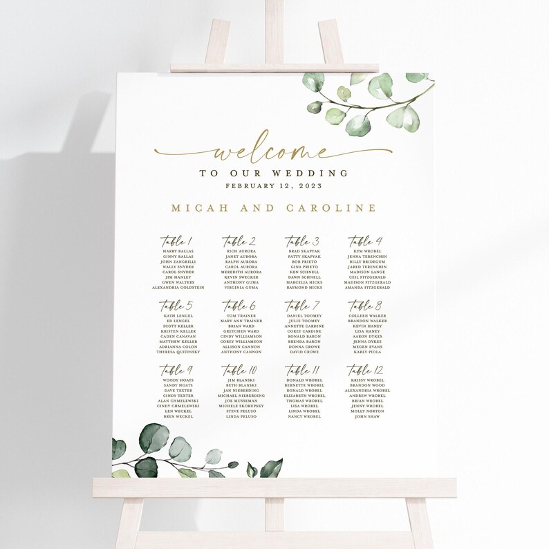 May include: A wedding seating chart with a white background and green eucalyptus leaves. The chart lists the names of guests assigned to each table number. The text at the top reads "Welcome to our wedding, February 12, 2023, Micah and Caroline."