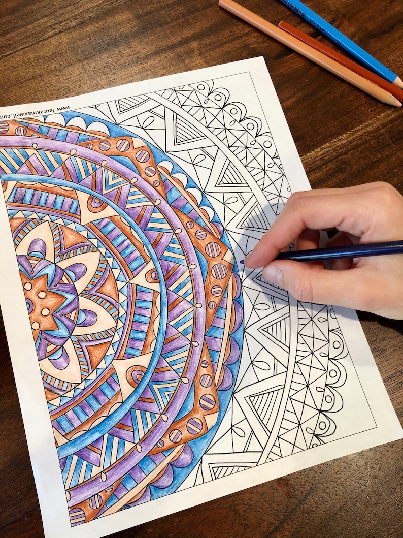 May include: A detailed mandala coloring page with intricate patterns in shades of blue, purple, and brown. The page is partially colored in with colored pencils, showing the progress of the coloring process.