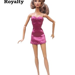 A pink strapless mini dress on a Fashion Royalty doll.  The dress features a fitted bodice with a gather at the bust and a short skirt. The dress has a satin finish and a subtle sheen.
