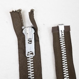 May include: Close-up of a brown zipper with a silver metal pull. The zipper teeth are silver, and the fabric is a dark brown colour. The zipper is partially open, showing the teeth and the slider.