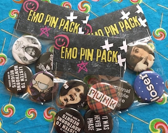 Puede incluir: Un conjunto de ocho botones emo con pasador en una bolsa de plástico transparente. Los botones presentan varios diseños con temática emo, incluyendo un logotipo de banda, un personaje de dibujos animados y texto que dice "Solía escuchar a Hawthorne Heights en la escuela secundaria". La bolsa está etiquetada como "Emo Pin Pack".