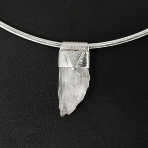 Peut inclure: Un collier en argent avec un pendentif en cristal transparent. Le pendentif est serti dans un cadre en argent avec un motif géométrique.