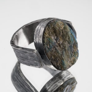 May include: A silver ring with a textured band and a large, oval-shaped, green and blue gemstone.