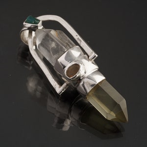 May include: A silver pendant with a clear quartz crystal and a green gemstone. The pendant is designed to hold a crystal point, which is visible in the image.