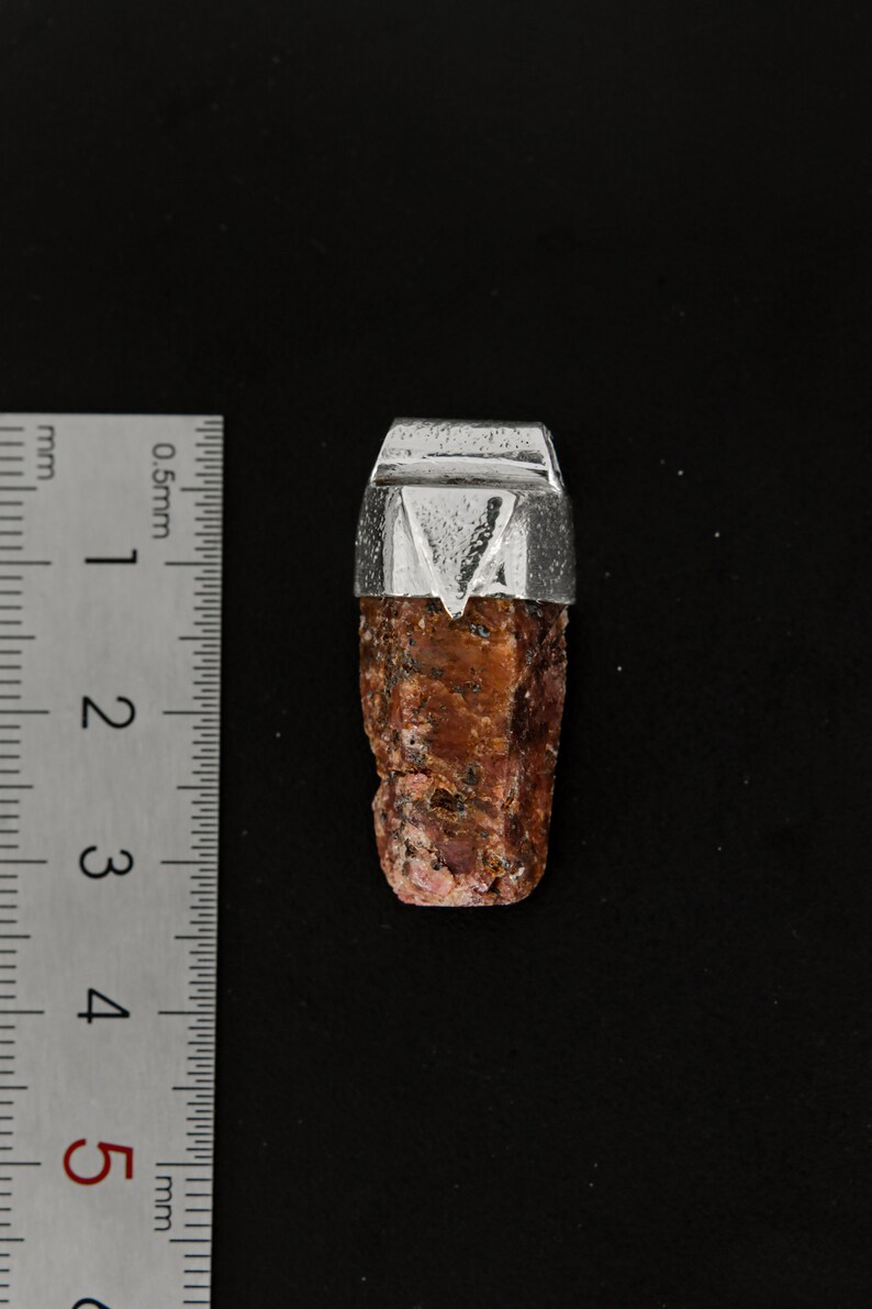 May include: A red gemstone pendant with a silver setting. The gemstone is a rough, natural shape and is approximately 2.5 cm long.