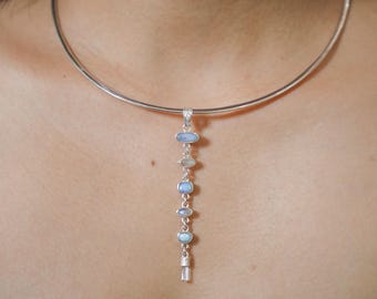 May include: A silver choker necklace with a pendant featuring a chain of oval-shaped blue stones and a crystal-like point at the end.