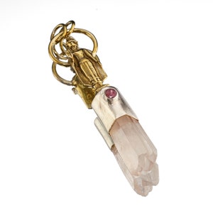 May include: Gold pendant featuring a small standing figure with a pink gemstone, attached to a clear quartz crystal.