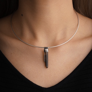 Könnte beinhalten: Eine silberne Choker-Kette mit einem Anhänger aus dunkelbraunem Kristall.
