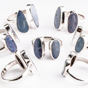 May include: Eight silver rings with blue opal stones. The rings are arranged in a circle on a white background.
