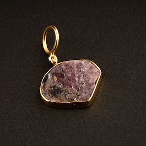 May include: A gold pendant featuring a pink and black gemstone with a rough, natural texture.