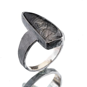 May include: A silver ring with a black, faceted, rutilated quartz stone. The ring has a hammered finish.