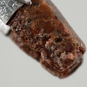 May include: A close-up of a dark red, faceted gemstone pendant with a silver setting. The gemstone has a rough, natural texture.