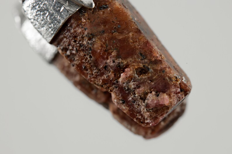 May include: A close-up of a dark red, faceted gemstone pendant with a silver setting. The gemstone has a rough, natural texture.