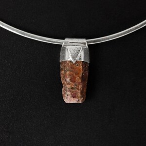 May include: A silver chain necklace with a pendant featuring a raw, reddish-brown gemstone set in a silver bezel.