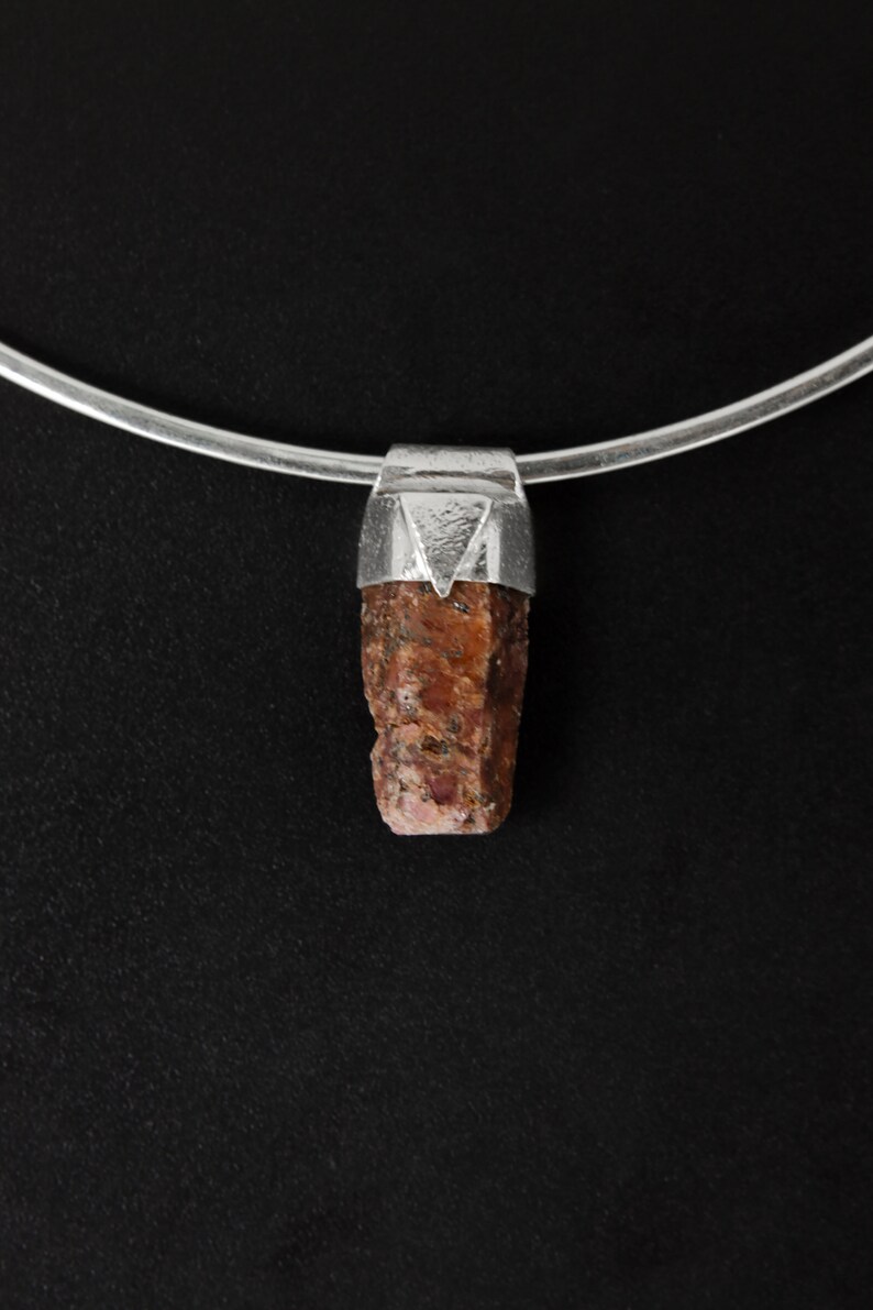 May include: A silver chain necklace with a pendant featuring a raw, reddish-brown gemstone set in a silver bezel.