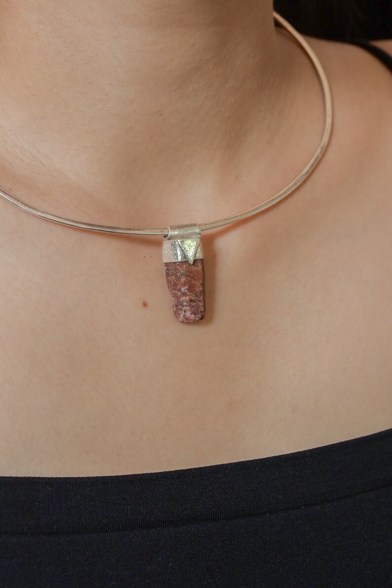 May include: A silver choker necklace with a pendant made of a rough, reddish-brown stone.
