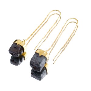 Puede incluir: Un par de pendientes de aro dorados con detalles de piedras negras. Las piedras son facetadas y tienen un aspecto áspero y natural.