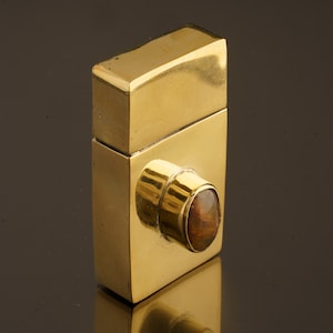 May include: A gold metal box with a hinged lid and a round, brown gemstone set into the front.