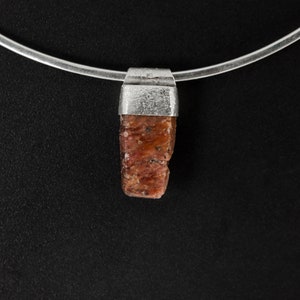 May include: A silver chain necklace with a pendant featuring a raw, reddish-brown gemstone.