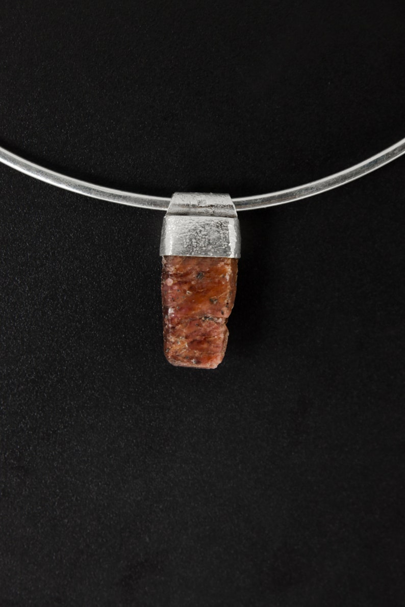 May include: A silver chain necklace with a pendant featuring a raw, reddish-brown gemstone.