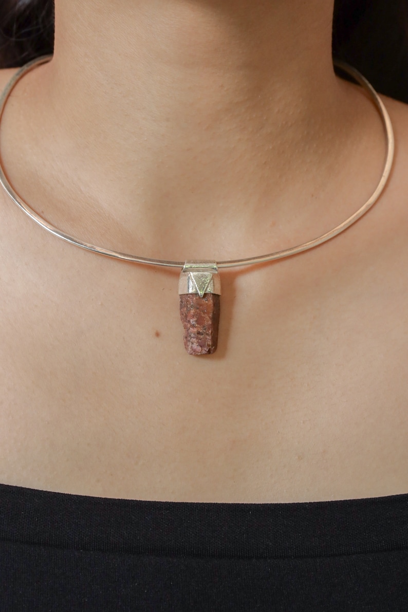 May include: A silver choker necklace with a pendant made of a rough, reddish-brown stone.