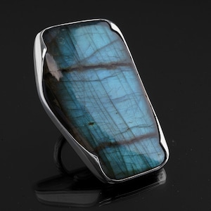 Puede incluir: Un anillo de plata con una gran piedra rectangular de labradorita azul. La piedra tiene una calidad iridiscente única.