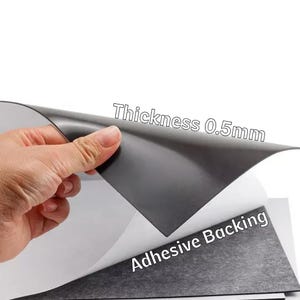 May include: A sheet of black magnetic material with adhesive backing is held up, revealing its white underside. The text "Thickness 0.5mm" is visible. The product is designed for various crafting and DIY projects.