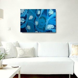 May include: Abstract painting with swirling blue and white patterns. The painting has a textured look and is framed in a white frame.