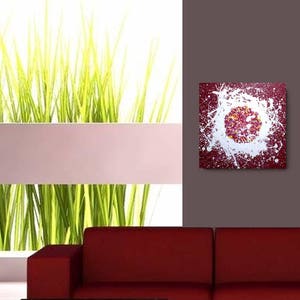 May include: Abstract painting with a white splatter design on a burgundy background. The splatter design creates a circular shape in the centre of the painting.