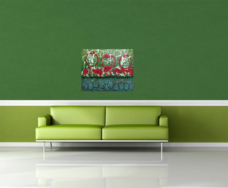 May include: Abstract art print with a green background and red, white, and blue circles. The print is framed and hanging on a green wall above a green sofa.