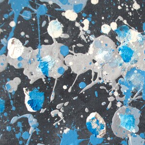 May include: Abstract art painting with blue, white, and gray paint splatters on a black background.