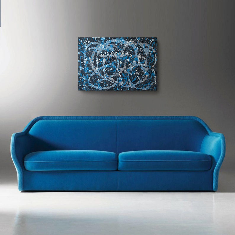 May include: A blue velvet sofa with a modern design. The sofa has a curved back and armrests. The sofa is in front of a gray wall with a black and white abstract painting hanging above it.